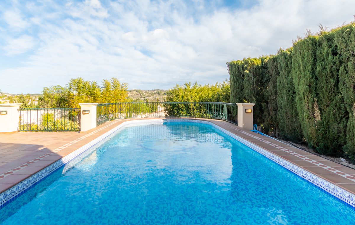Piscine extérieure avec mosaïque bleue, bordure en terre cuite et garde-corps en fer forgé, bordée par une haute haie de cyprès pour plus d'intimité.
