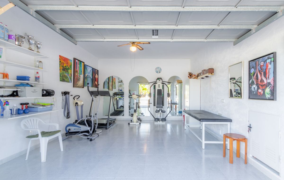 Salle de sport privée dans un garage aménagé avec carrelage, équipée d'appareils de cardio, d'une station de musculation et d'une table de massage.