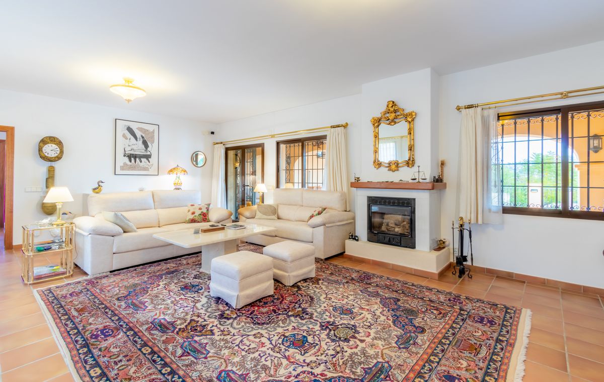 Salon spacieux avec sol en terre cuite, cheminée surmontée d'un miroir doré et canapés blancs disposés sur un grand tapis de style classique.