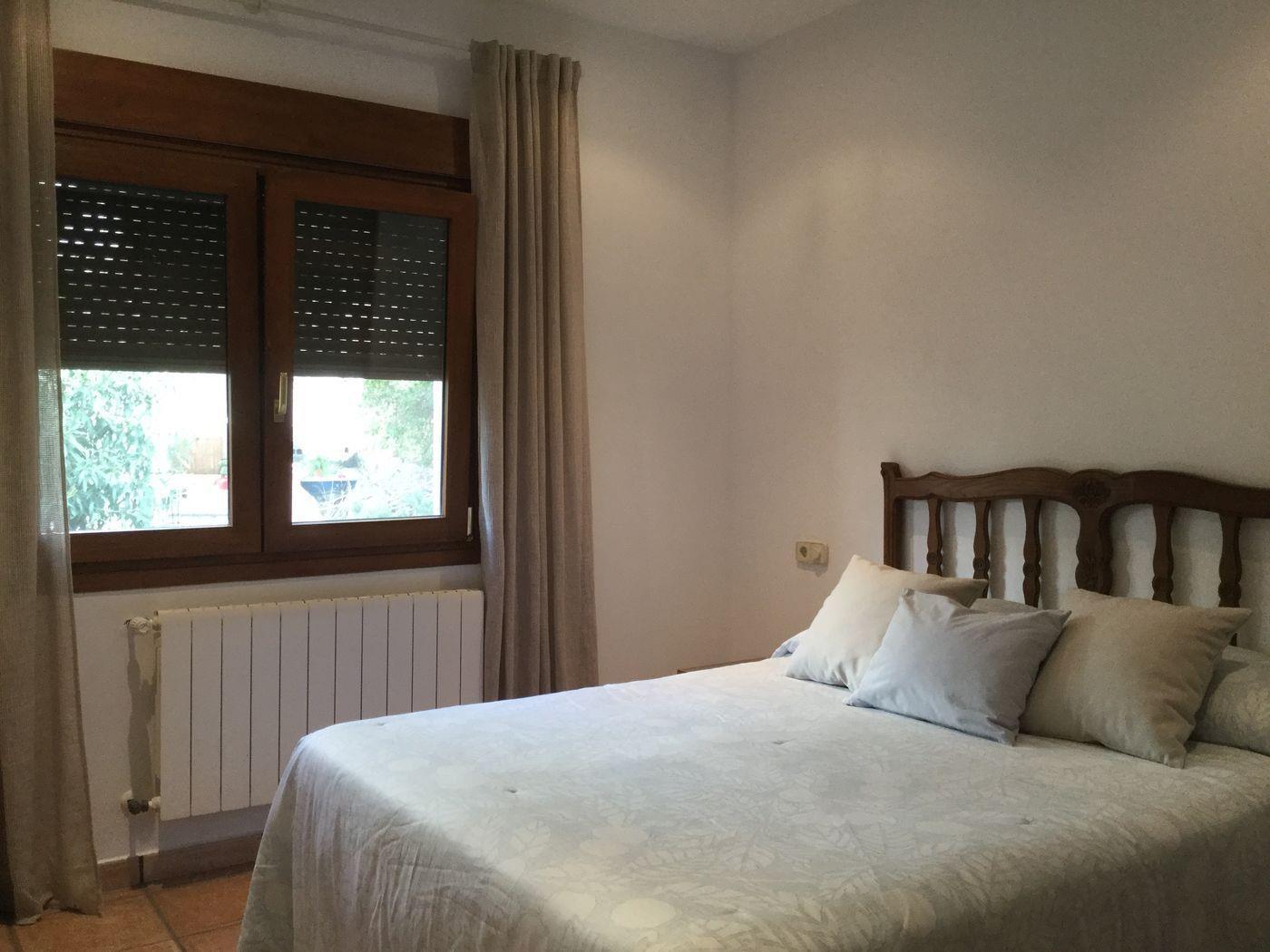 Chambre à coucher avec lit double, tête de lit en bois sculpté, fenêtre à cadre en bois avec volets roulants et radiateur blanc mural.