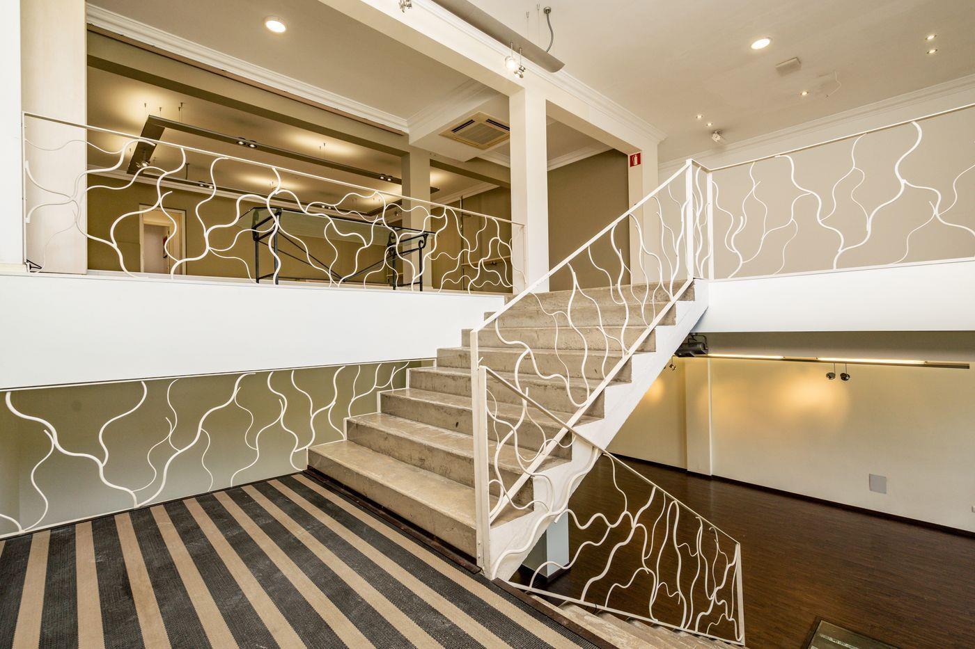 Escalier intérieur moderne avec marches en pierre et garde-corps métallique blanc au motif organique, reliant le rez-de-chaussée à la mezzanine.