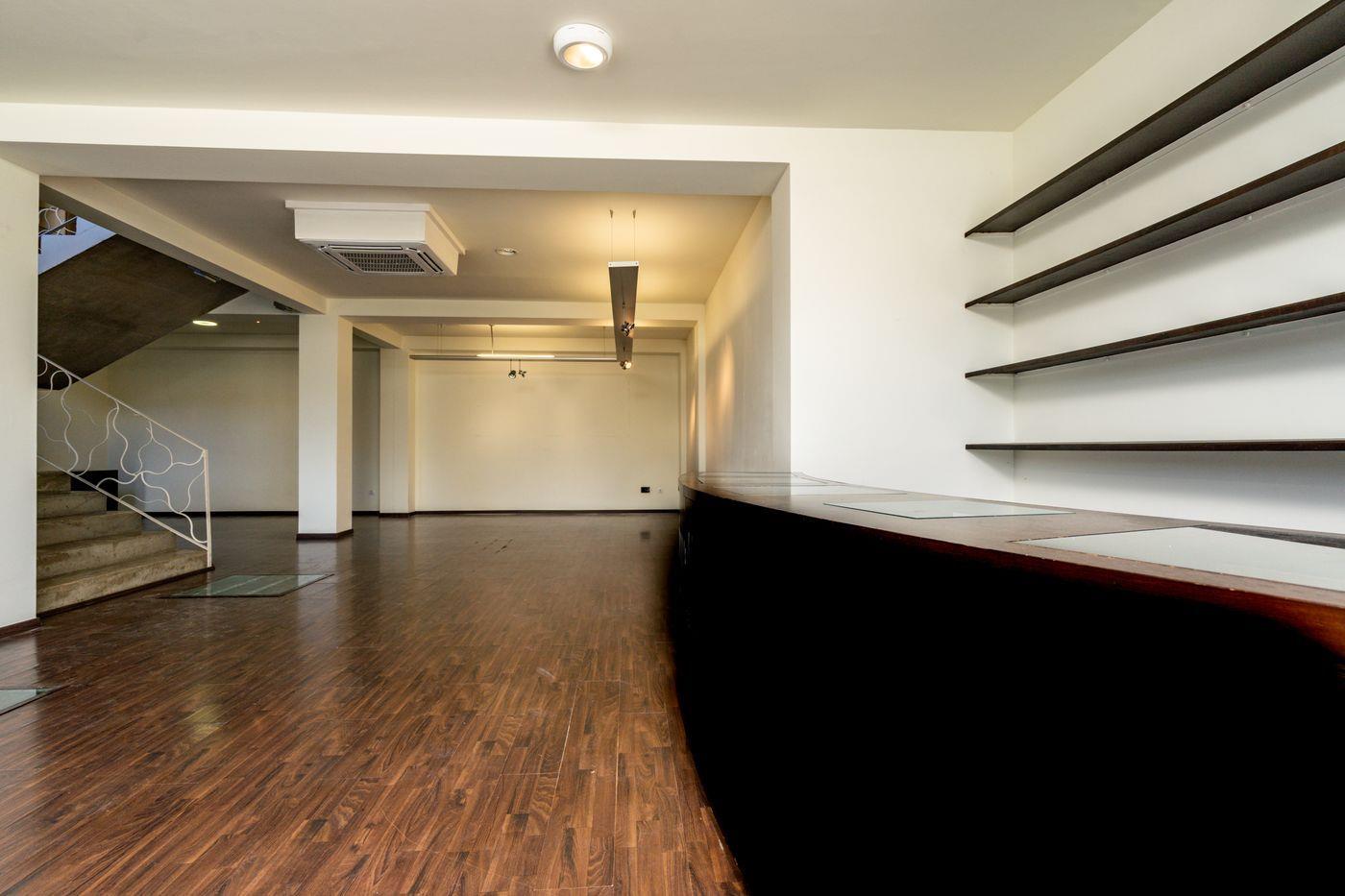 Espace commercial ouvert avec parquet sombre, comptoir de réception courbé, étagères murales et escalier avec rampe métallique ornementale.