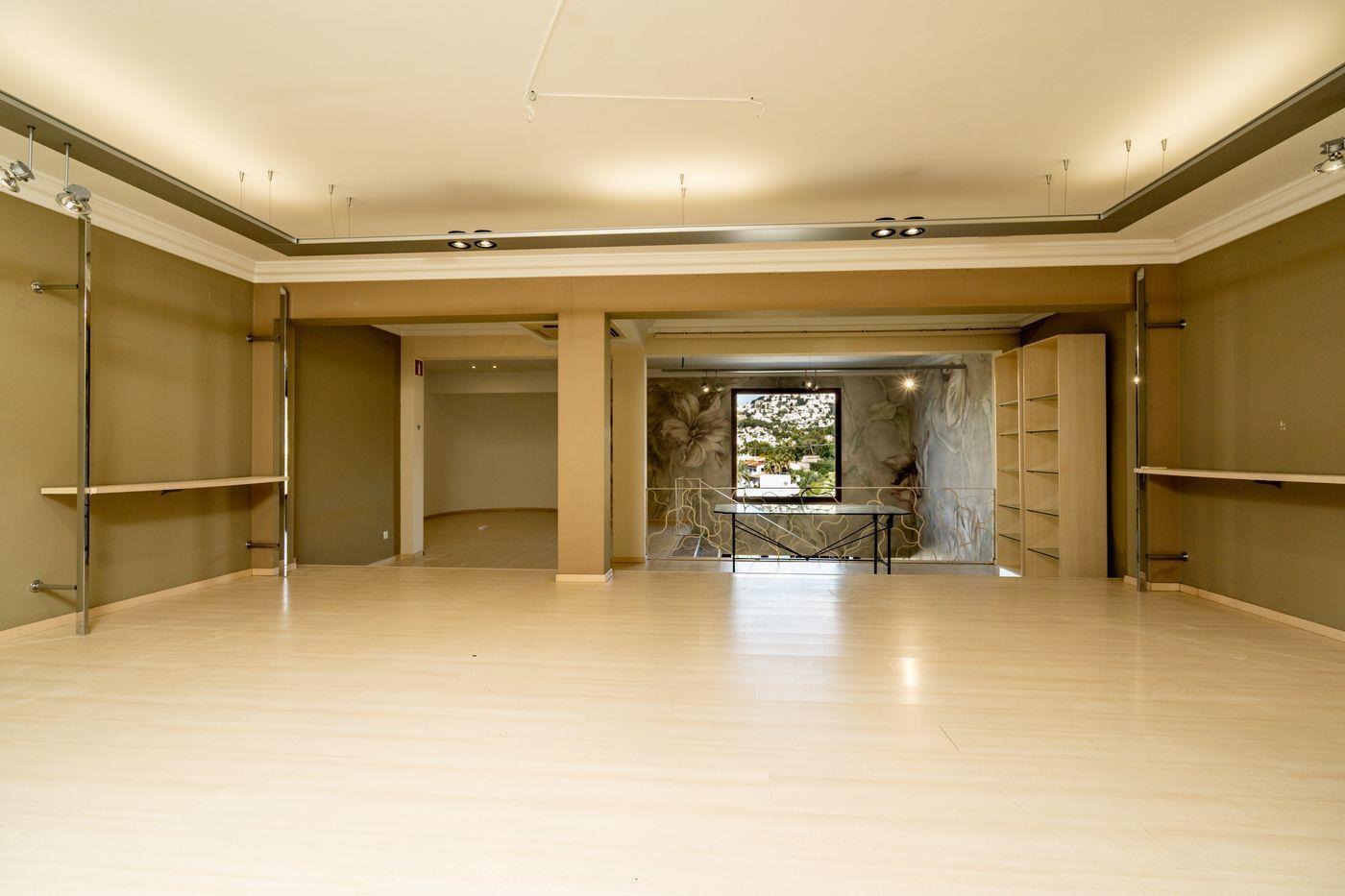 Espace commercial spacieux avec parquet clair, éclairage indirect au plafond et présentoirs chromés. Un mur décoratif et une fenêtre offrant une vue dégagée sont visibles au fond.