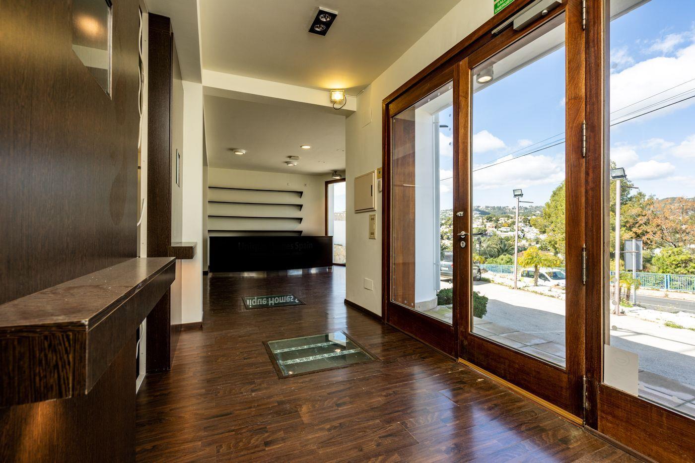 Espace d'entrée avec parquet stratifié sombre, dalle de verre au sol et grandes portes vitrées en bois ouvrant sur un comptoir de réception et des étagères.