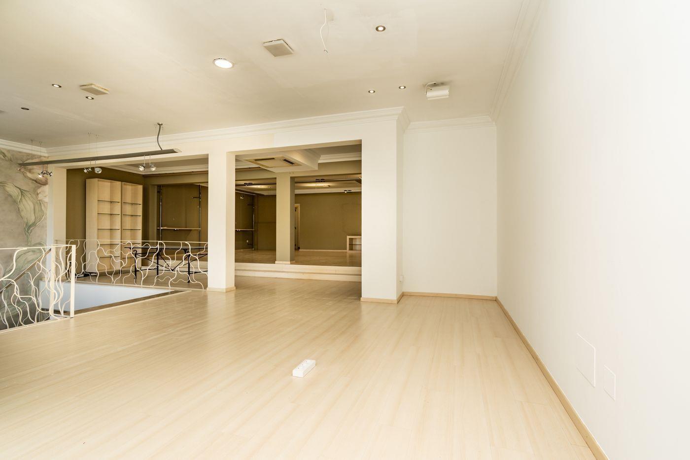 Espace ouvert spacieux avec parquet clair, éclairage encastré au plafond et garde-corps décoratif en métal blanc surplombant l'étage inférieur.