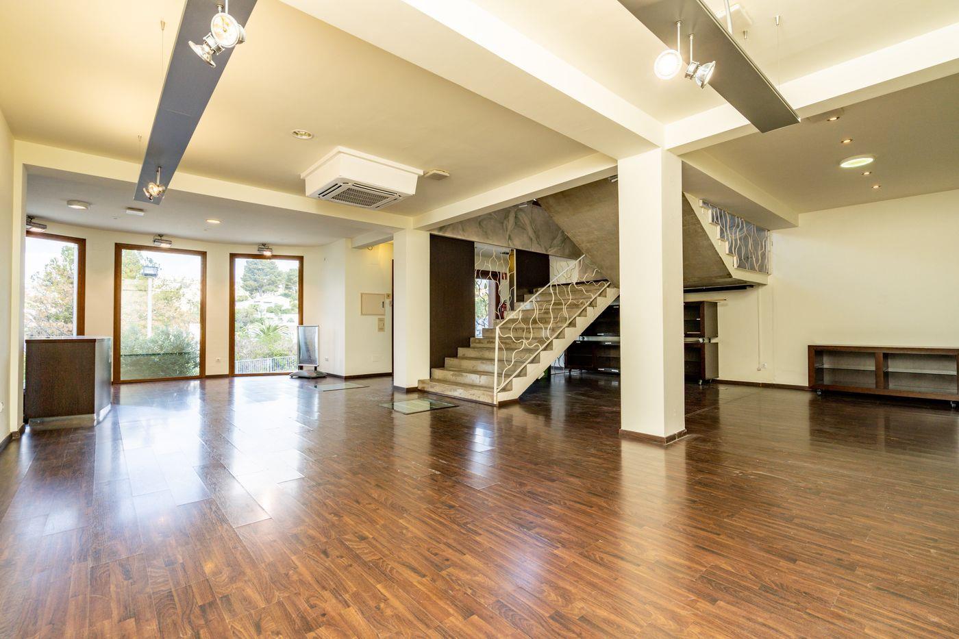 Espace ouvert spacieux avec parquet sombre, escalier central en béton doté d'une rampe décorative blanche et éclairage sur rails au plafond.