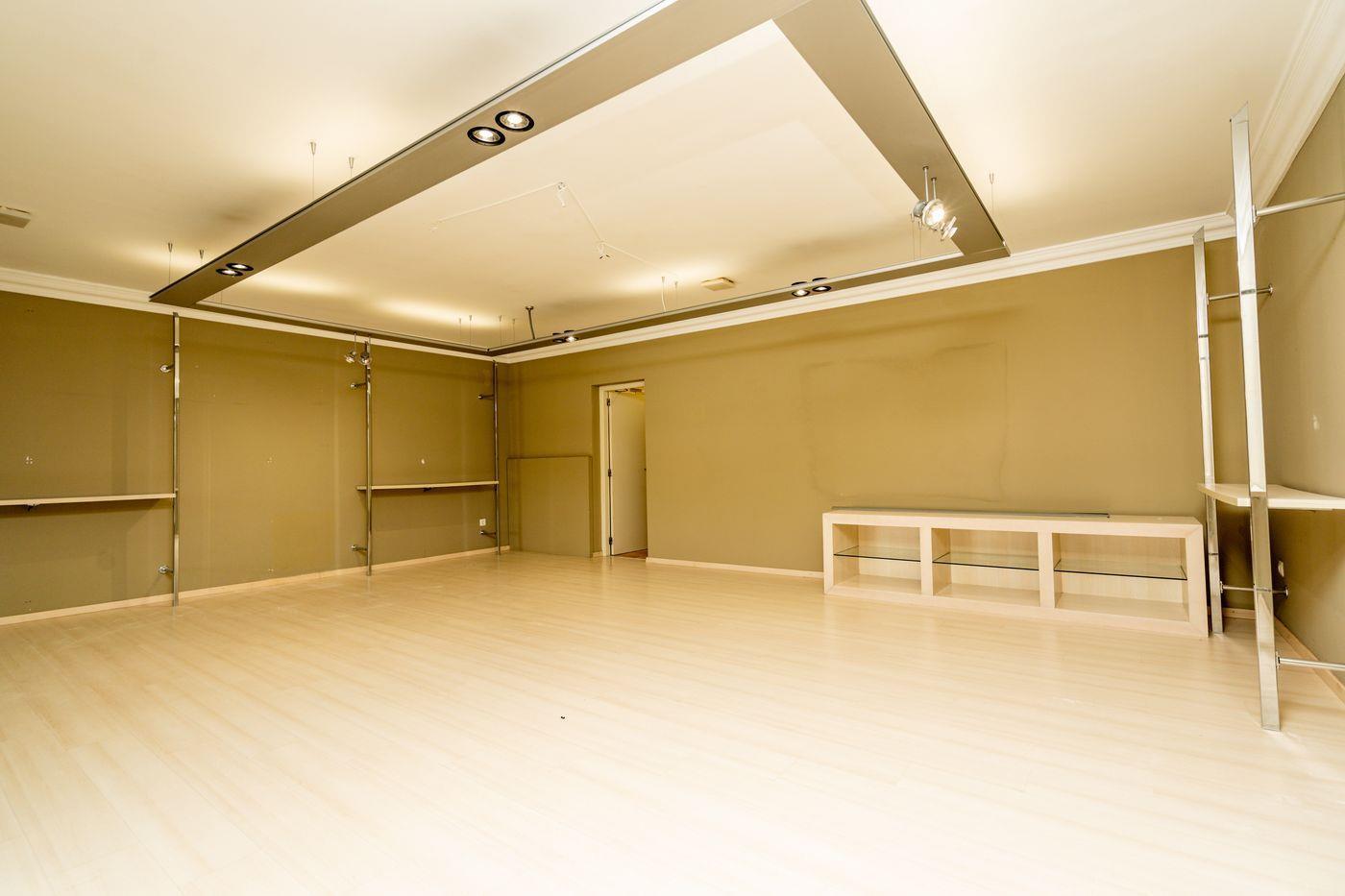 Espace spacieux avec parquet clair, plafond à caisson avec spots intégrés et étagères métalliques sur des murs aux tons olive.