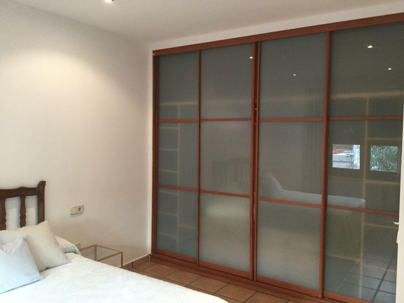 Grand placard intégré avec quatre portes coulissantes en verre dépoli et cadres en bois. La chambre dispose d'un sol en terre cuite et d'un éclairage encastré.