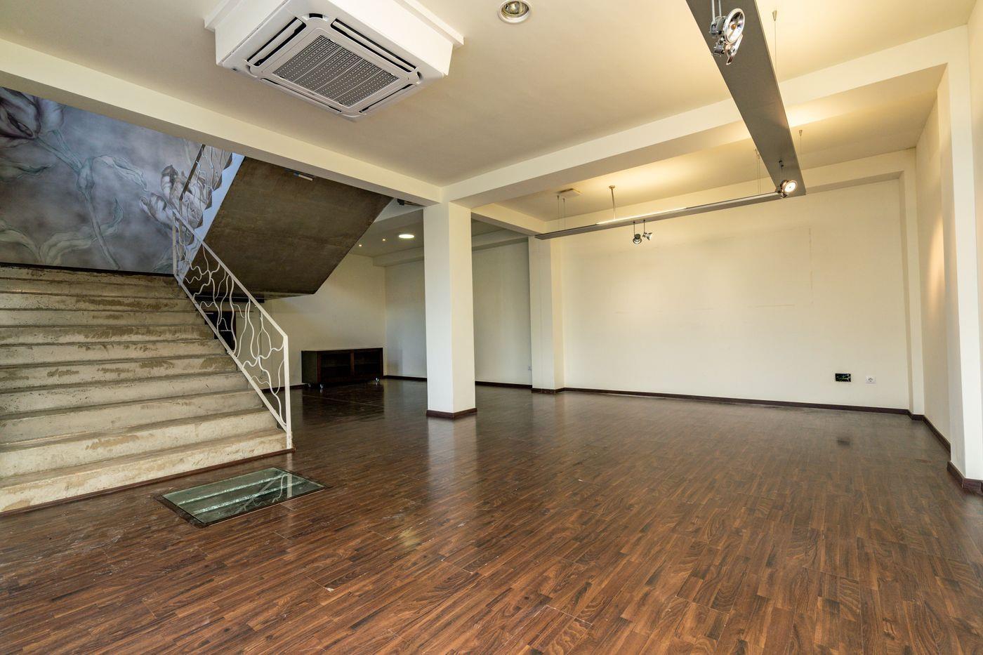 Intérieur à aire ouverte avec parquet sombre, escalier en pierre avec rampe blanche décorative et climatisation encastrée au plafond.