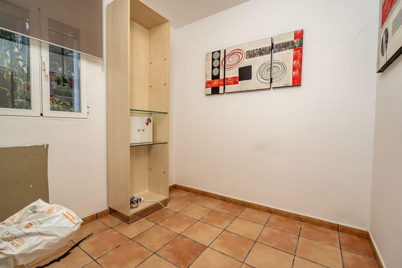 Petite pièce intérieure avec sol en terre cuite, étagère haute en bois clair avec tablettes en verre et triptyque d'art abstrait au mur.