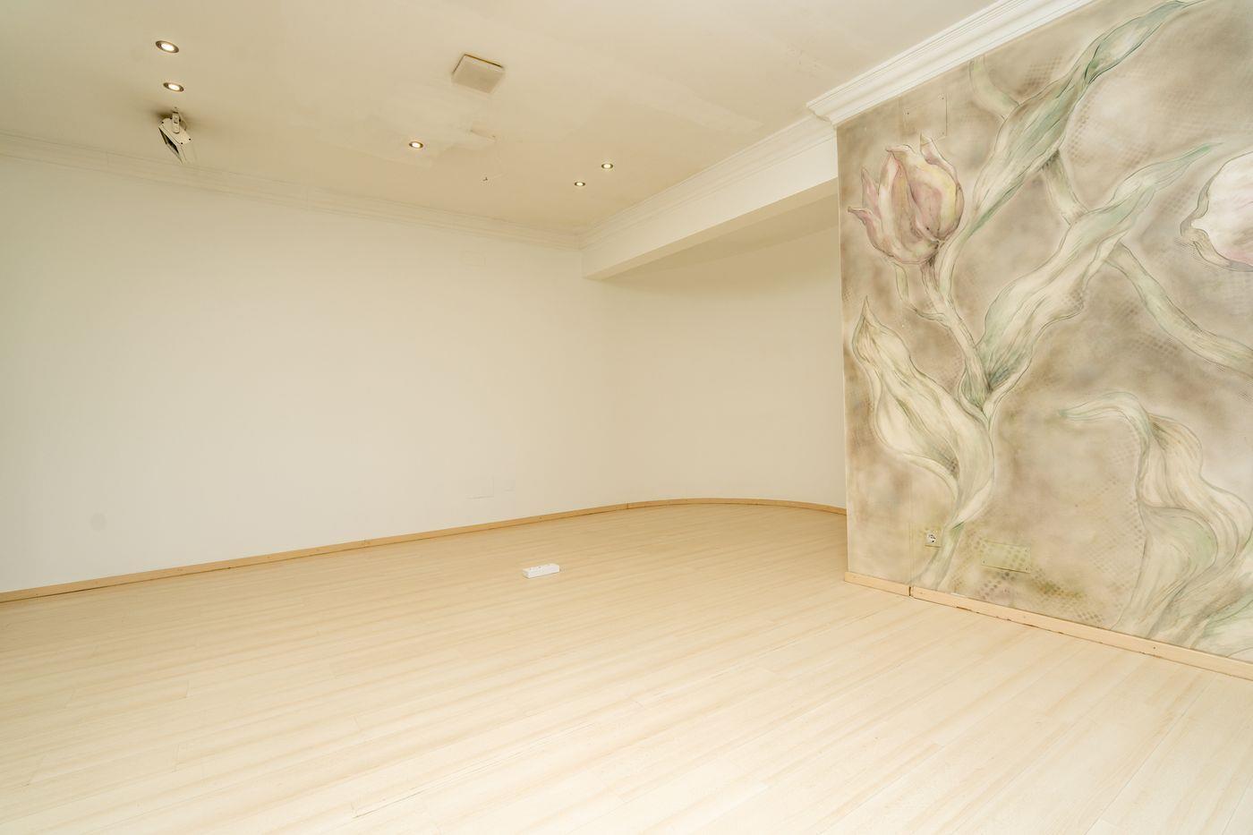 Pièce spacieuse avec parquet clair, spots encastrés au plafond et une fresque murale florale décorative sur le mur latéral.