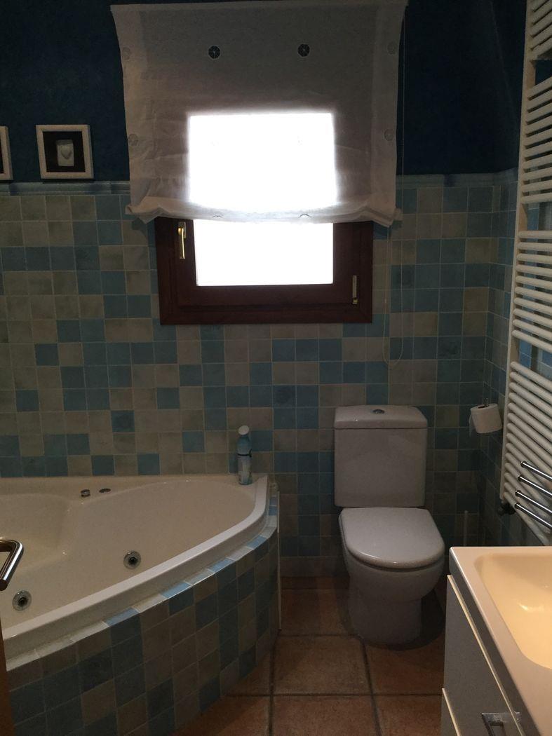 Salle de bain avec baignoire balnéo d'angle, carrelage en mosaïque bleue et radiateur sèche-serviettes blanc. Fenêtre en bois offrant une lumière naturelle.