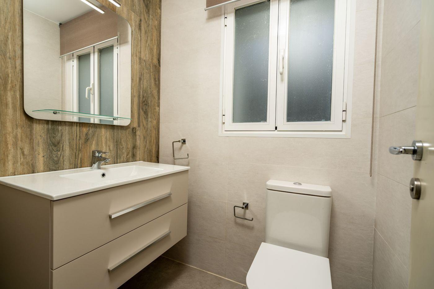Salle de bain moderne avec meuble vasque blanc, mur d'accent effet bois, grand miroir et fenêtre en verre dépoli.
