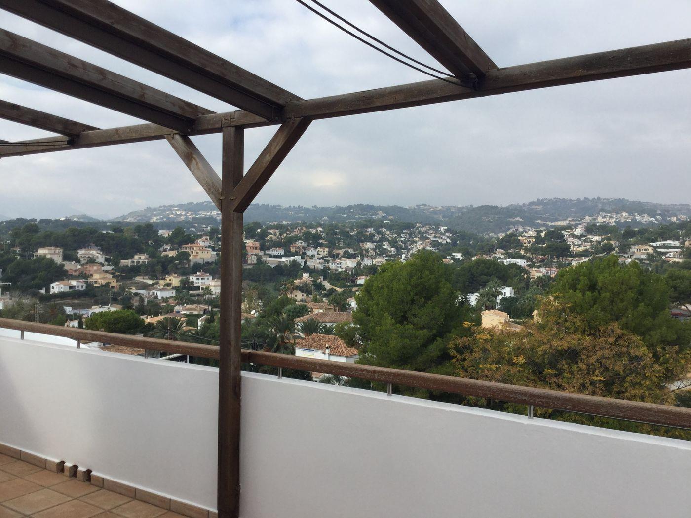 Terrasse surélevée avec pergola en bois sombre et garde-corps, offrant une vue panoramique sur une vallée résidentielle et sa végétation.