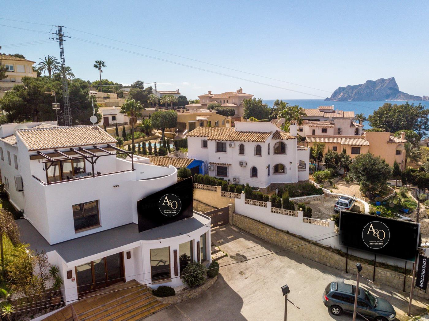 Vue aérienne d'une villa méditerranéenne blanche avec façade incurvée, terrasse sur le toit avec pergola en bois et vue sur la mer et le Peñón de Ifach.