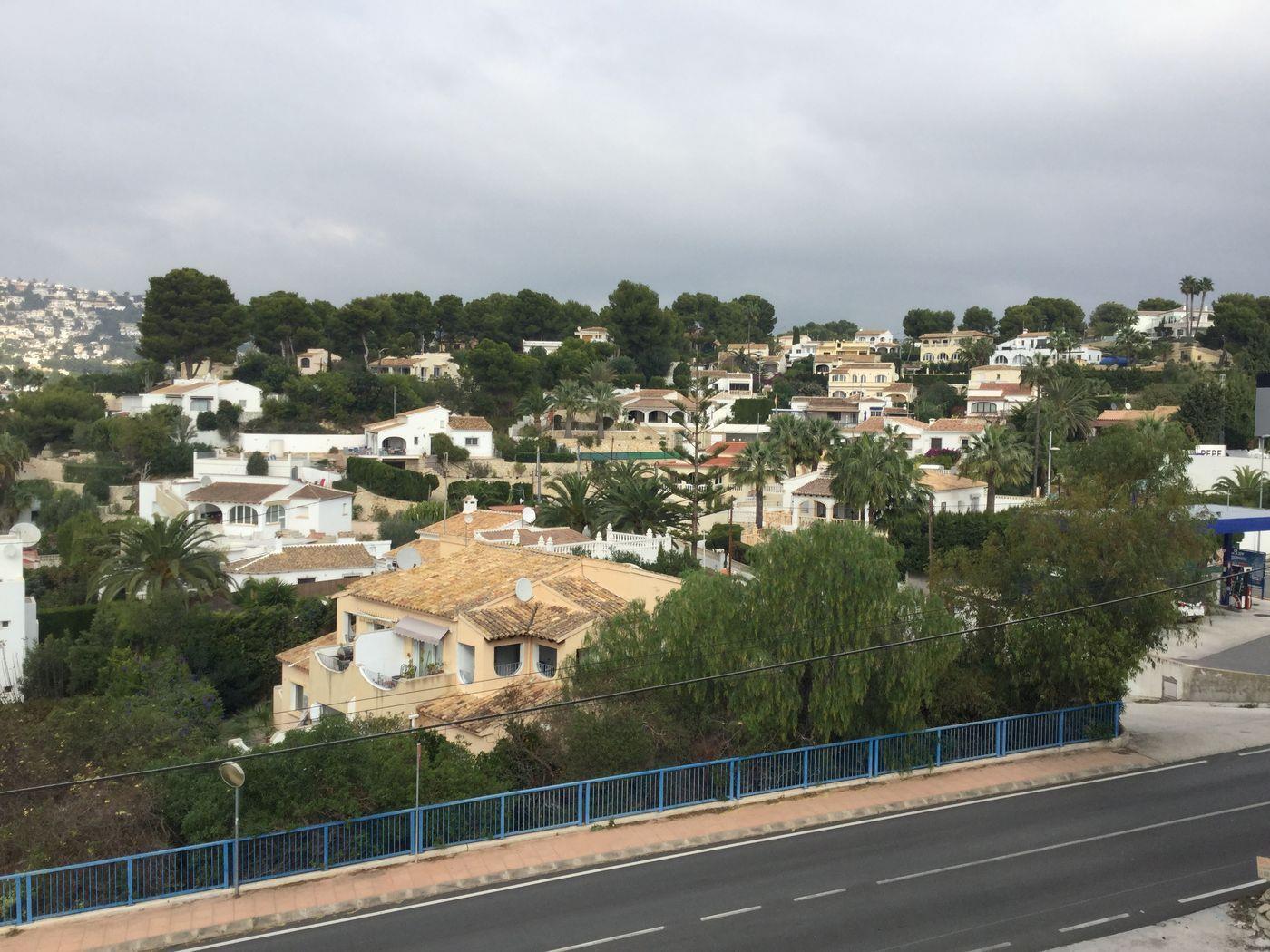 Vue surélevée d'un quartier résidentiel méditerranéen avec des villas blanches aux toits de tuiles, entourées de pins et de palmiers.