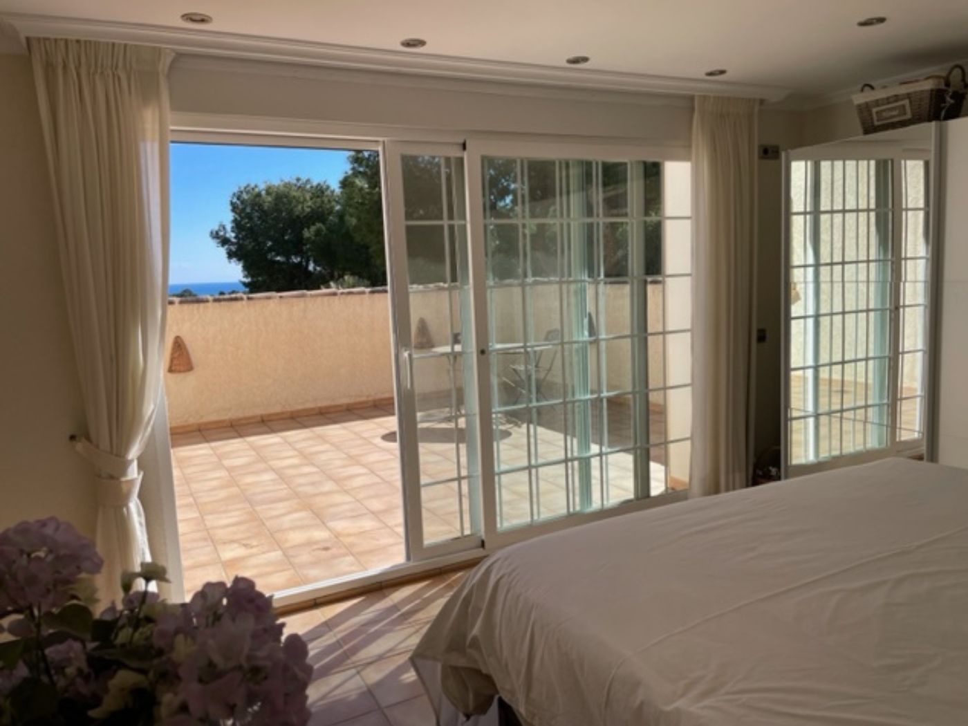 Chambre à coucher avec de grandes baies vitrées coulissantes ouvrant sur une terrasse carrelée privée offrant une vue sur la mer.