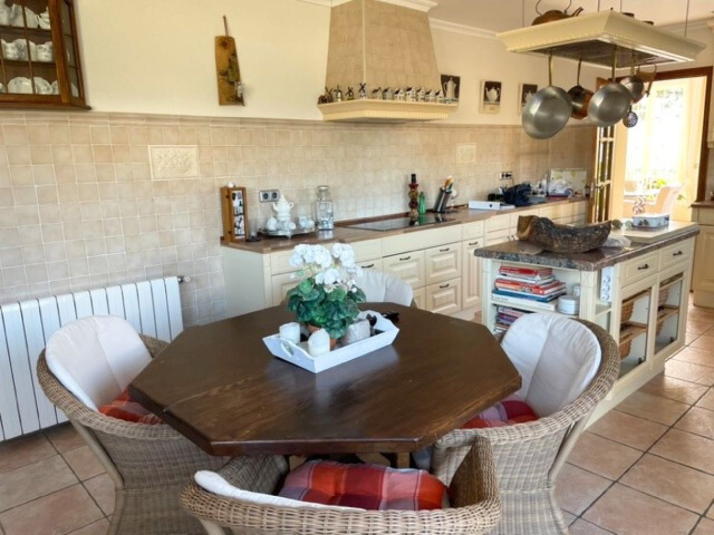 Cuisine avec table octogonale en bois, chaises en osier et îlot central avec plan de travail en marbre, accompagnée de meubles de rangement de style rustique.