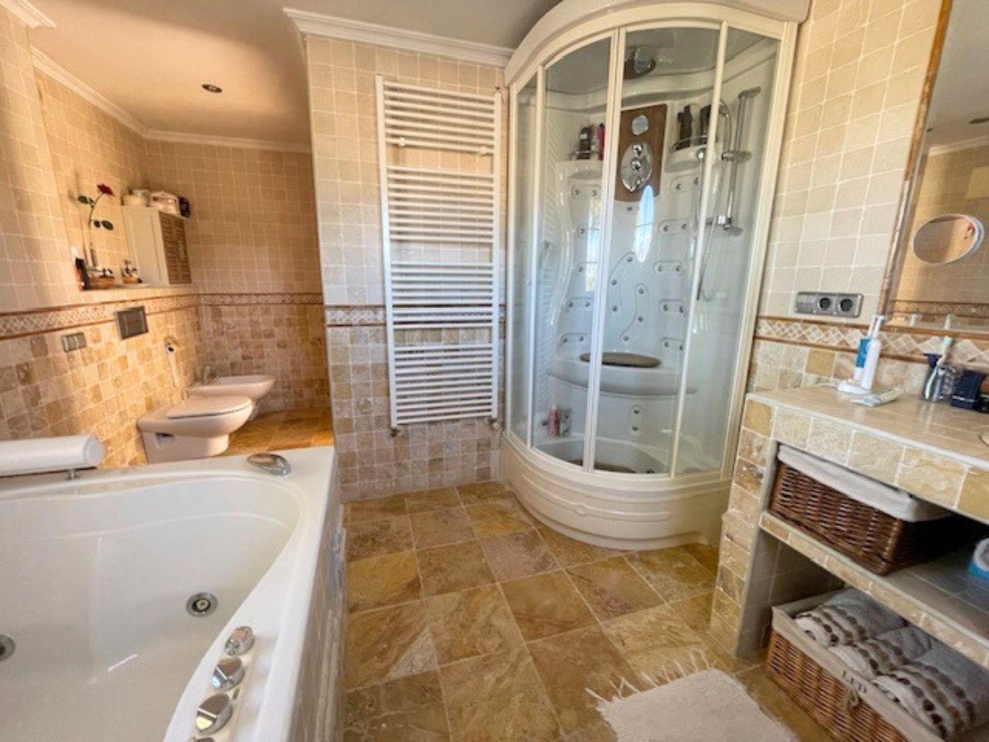 Salle de bain équipée d'une cabine de douche d'angle avec hydromassage, d'une baignoire et de carrelage en pierre naturelle. Comprend un sèche-serviettes blanc.