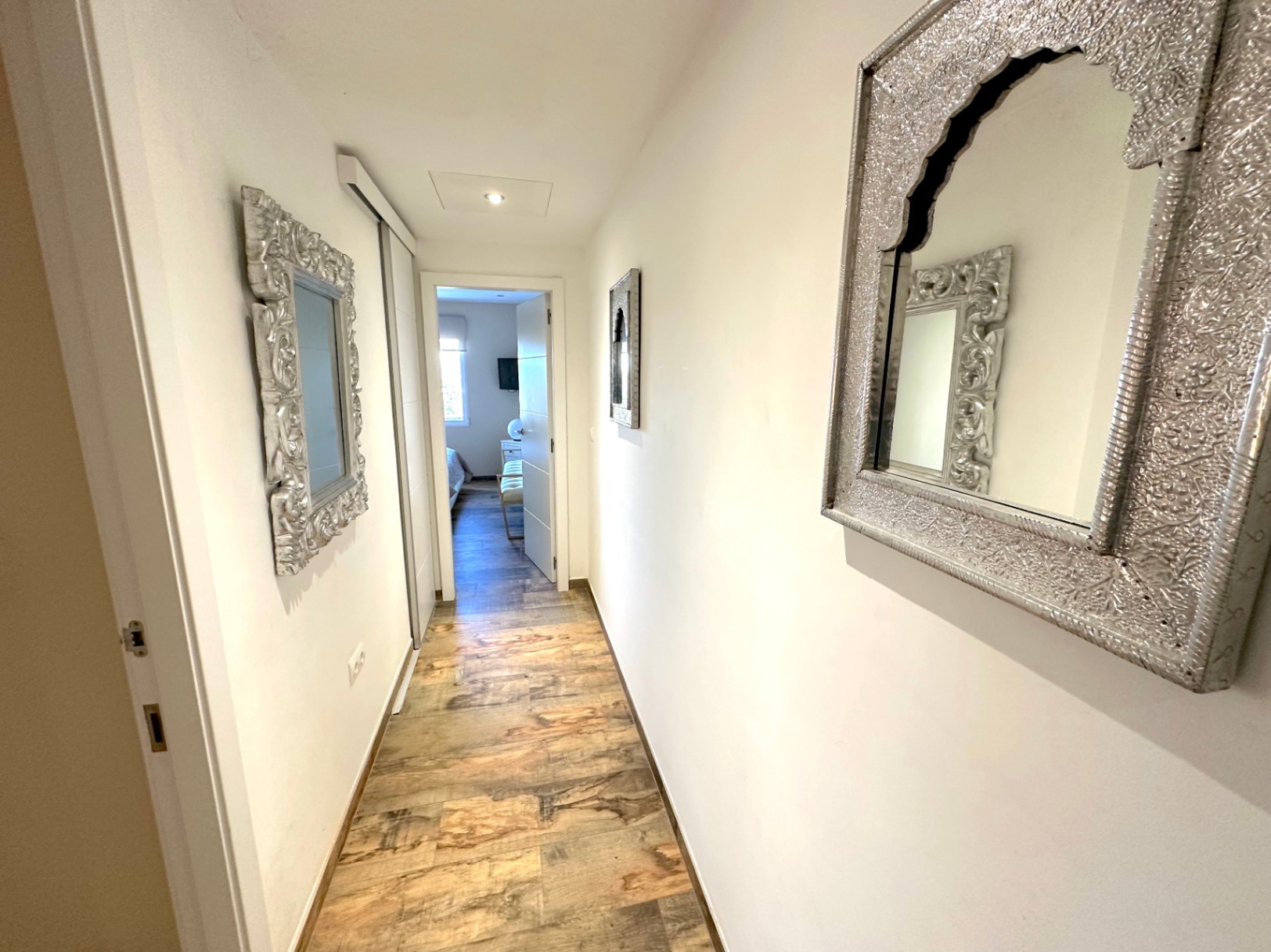 Couloir lumineux avec sol en grès cérame imitation bois, miroirs aux cadres argentés sculptés et placards intégrés aux finitions blanches.