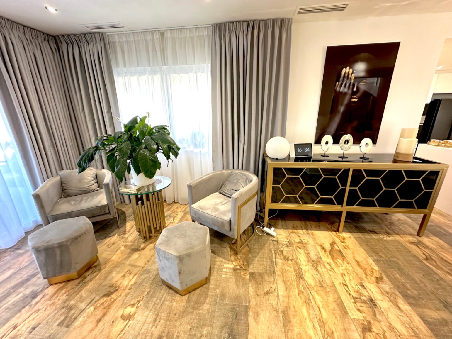 Espace détente avec fauteuils en velours gris, poufs hexagonaux et buffet design aux motifs géométriques dorés sur un sol en bois naturel.