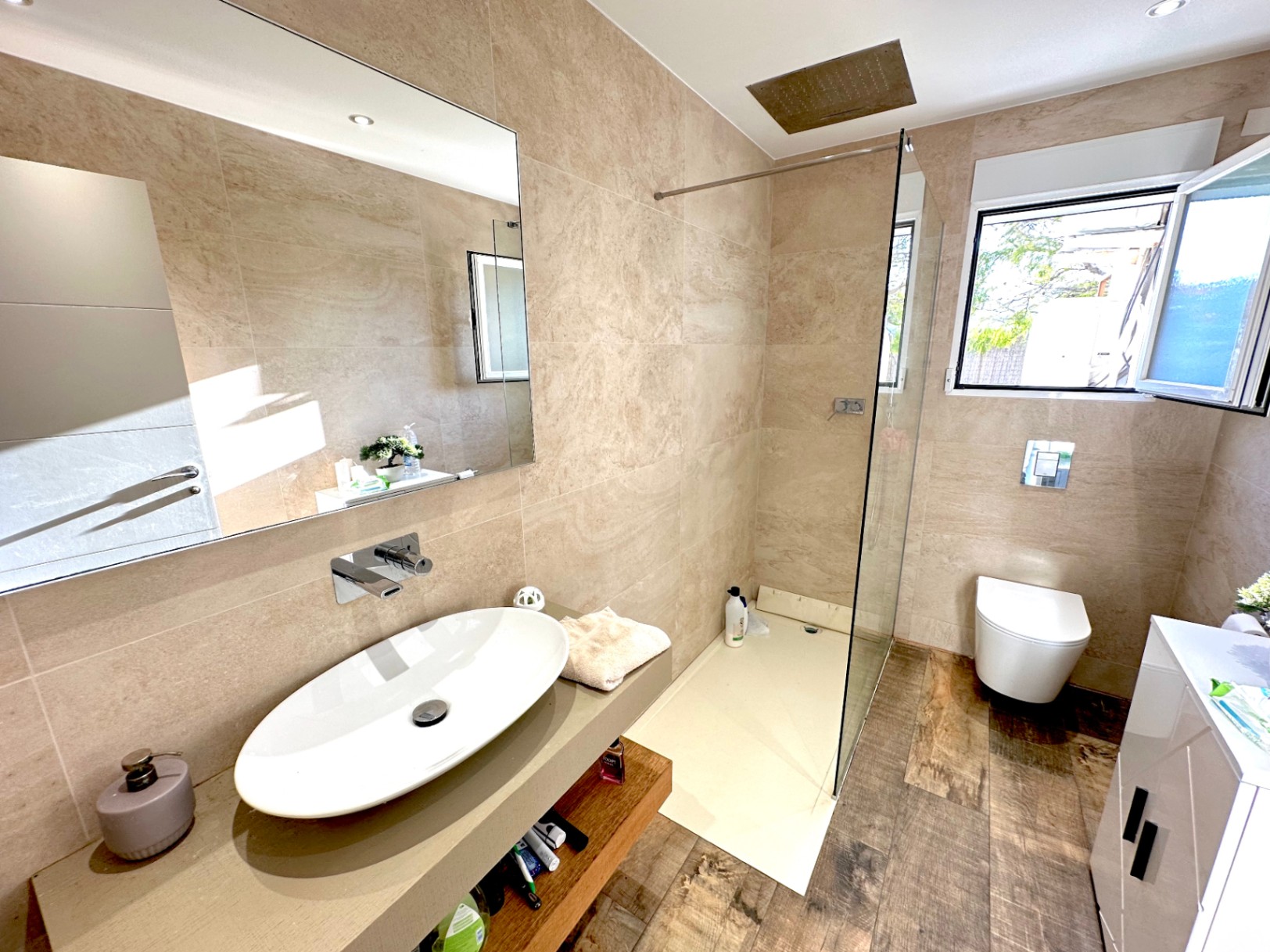 Salle de bain moderne avec vasque à poser, robinetterie murale et douche à l'italienne. Revêtement mural en grès cérame beige et sol en carrelage à l'aspect bois chaleureux.