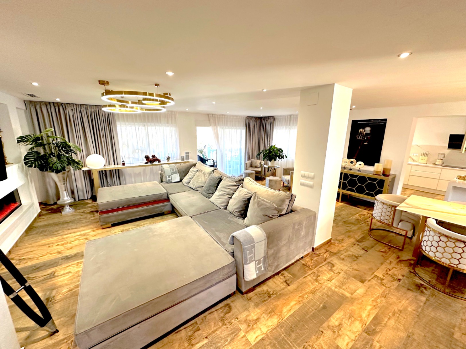 Salon à aire ouverte avec parquet, grand canapé modulaire gris, cheminée moderne et lustre circulaire doré au design contemporain.