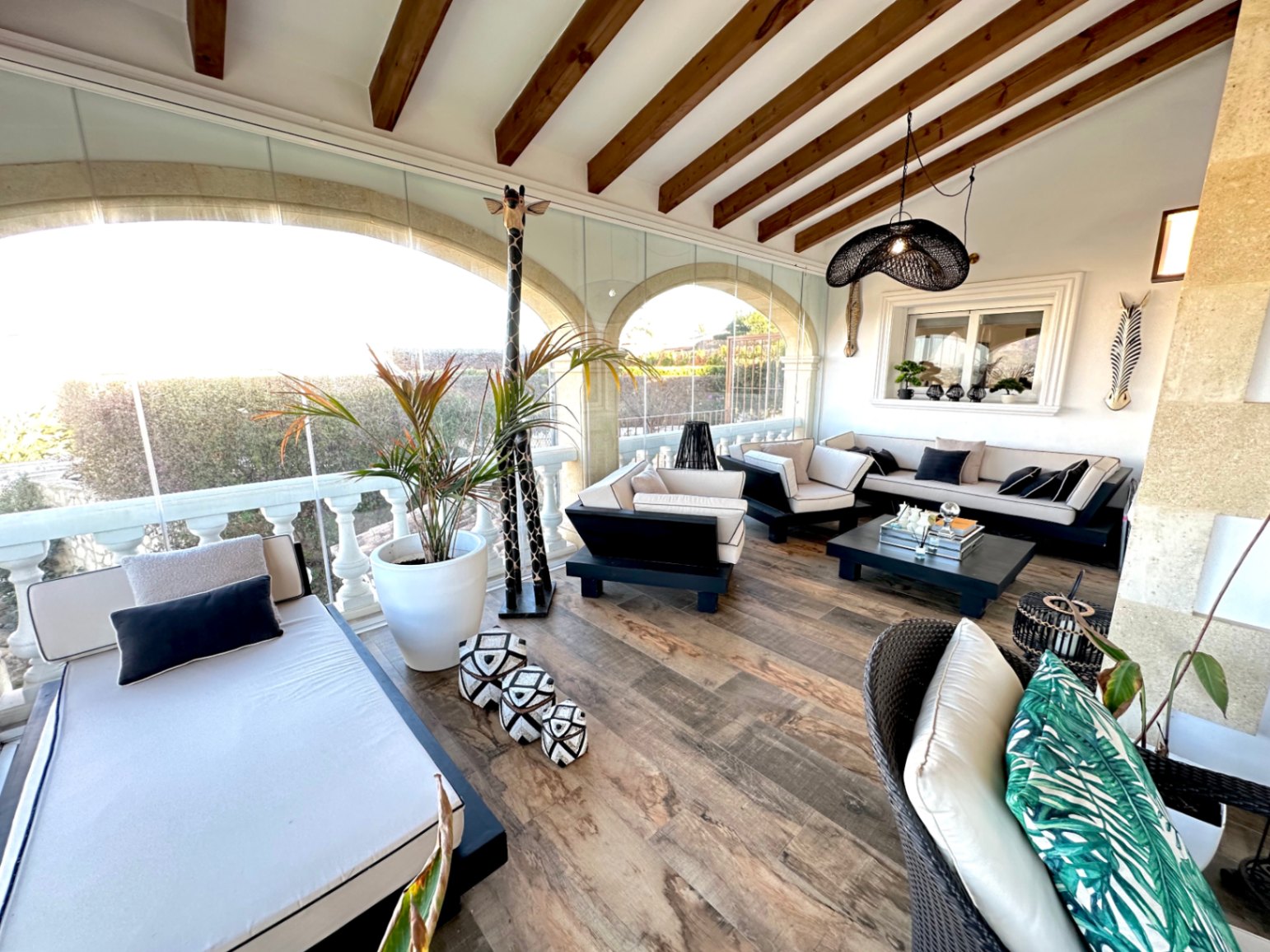 Terrasse vitrée avec poutres en bois apparentes, mobilier de salon contemporain noir et blanc et arches traditionnelles en pierre.