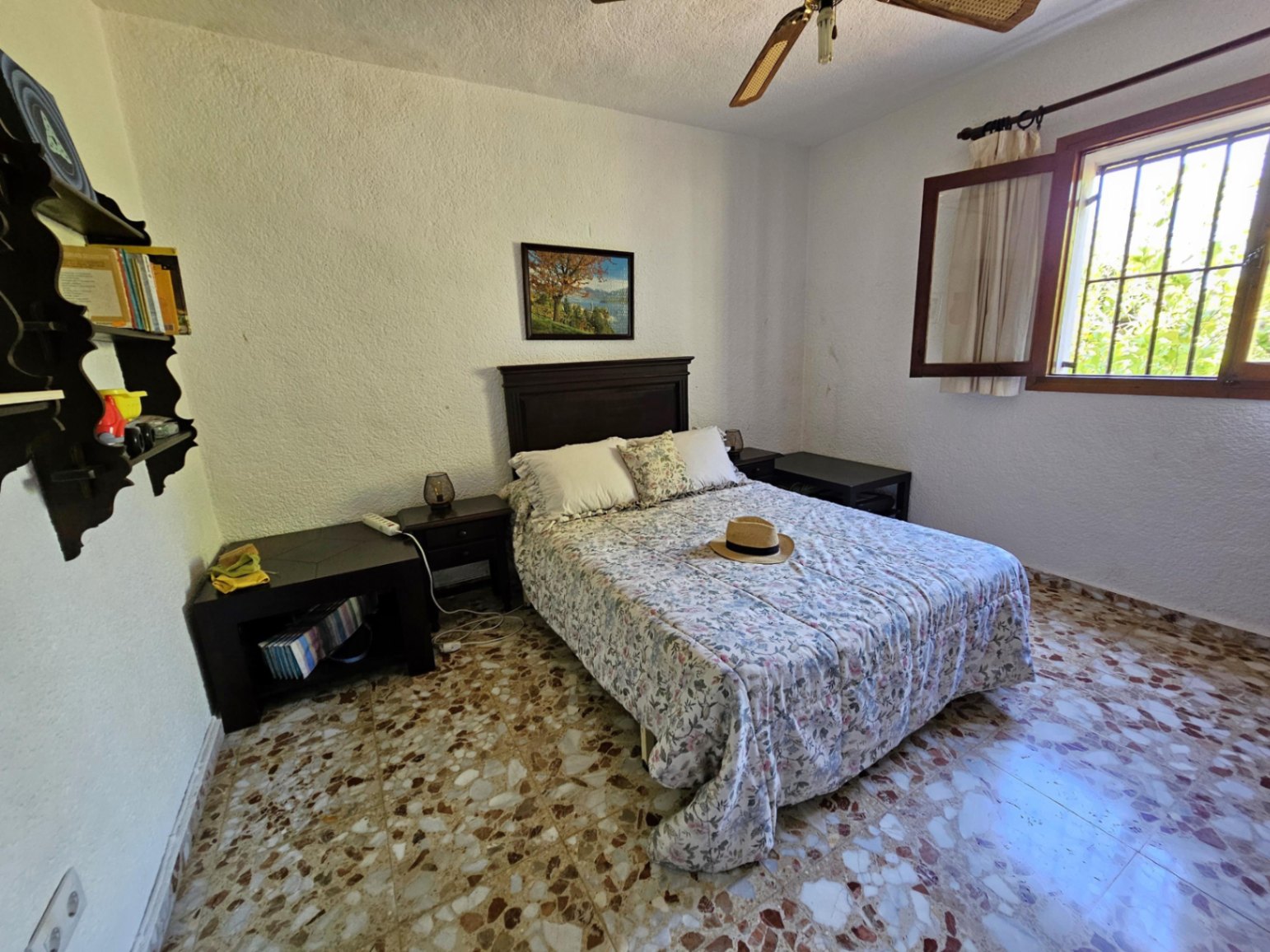 Chambre à coucher avec sol en terrazzo d'origine, tête de lit en bois sombre et fenêtre à cadre en bois offrant une luminosité naturelle constante.