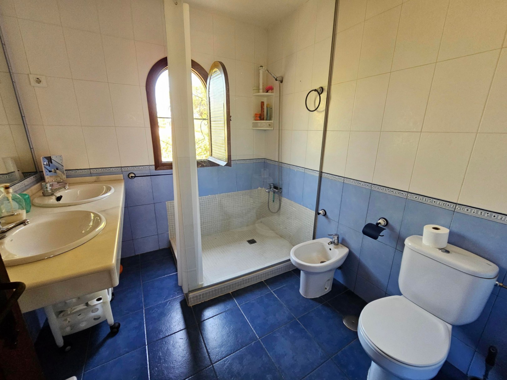 Salle de bain avec double vasque en marbre, douche à l'italienne en mosaïque, bidet et WC. Fenêtre cintrée en bois et carrelage mural bicolore bleu et blanc.