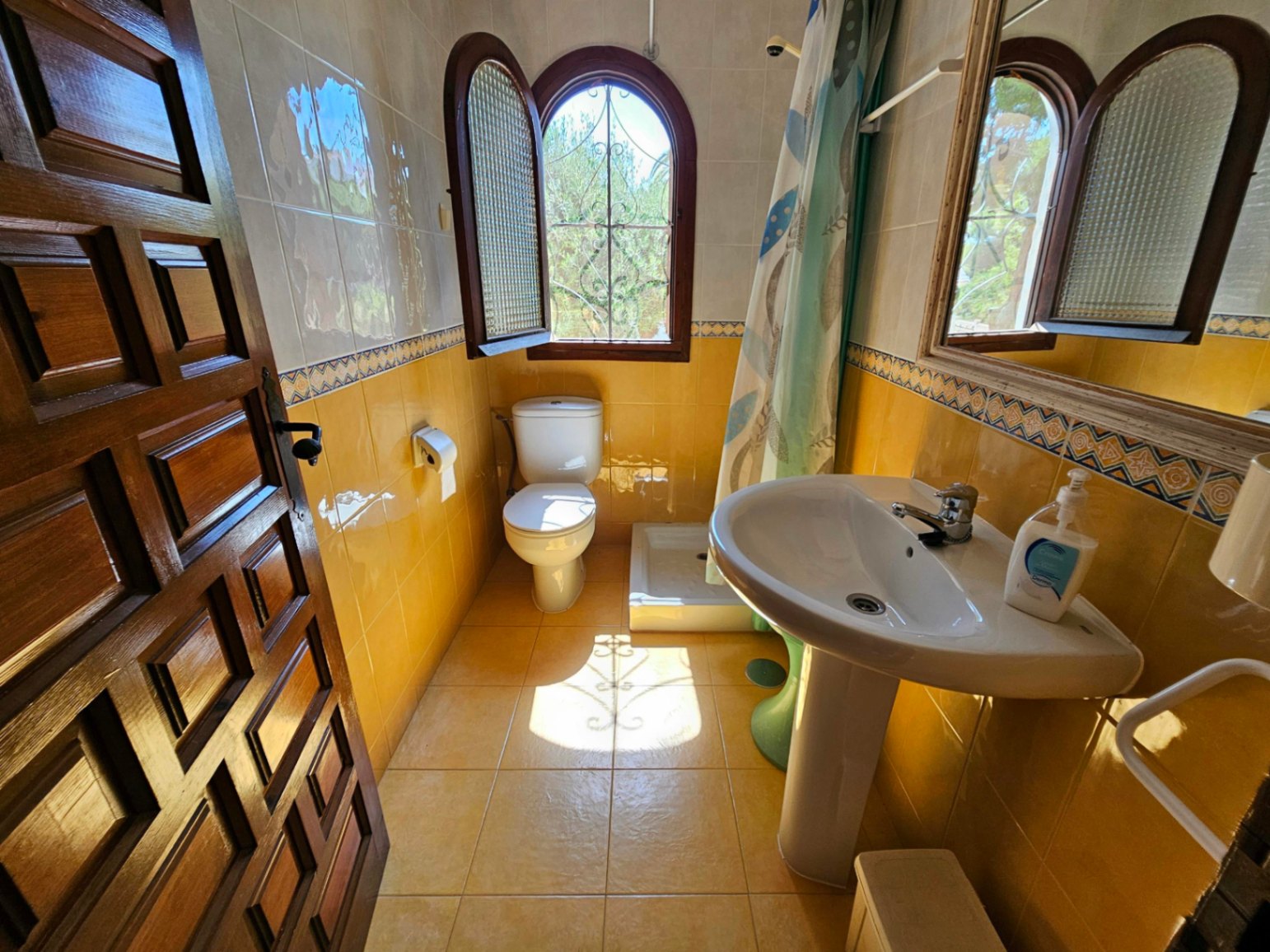 Salle de bain de style traditionnel avec carrelage jaune, lavabo sur colonne blanc et fenêtre cintrée en bois avec ferronnerie.