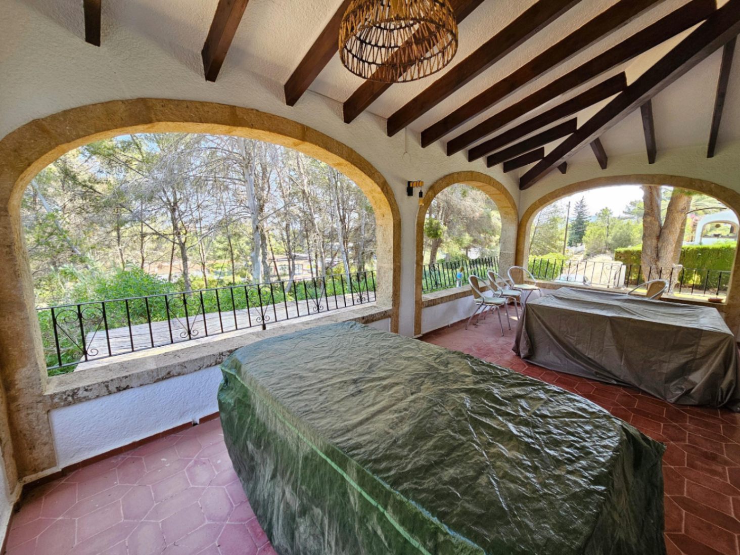 Terrasse couverte avec arches en pierre, poutres apparentes en bois sombre et sol en terre cuite offrant une vue sur la forêt environnante.