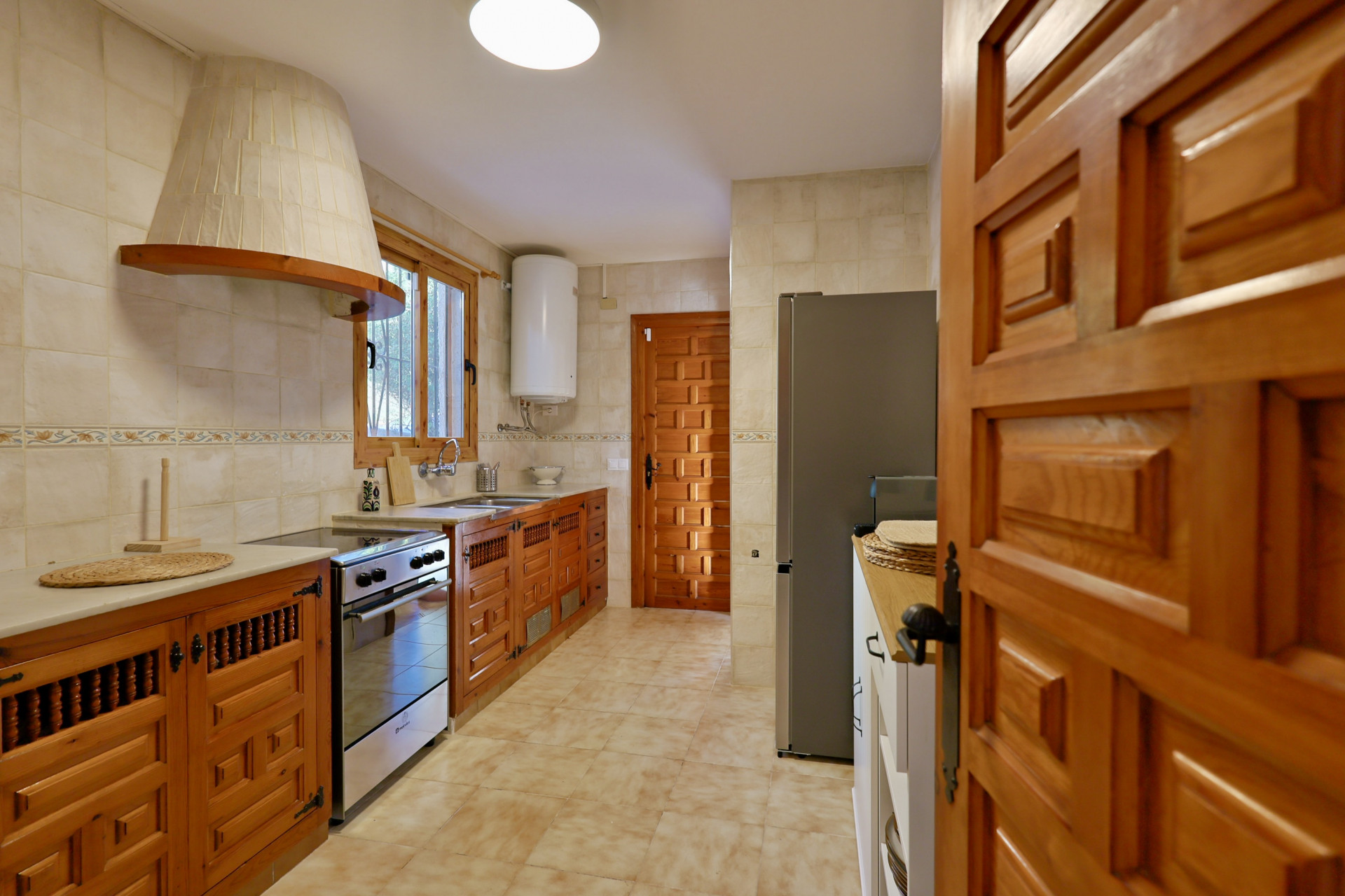 Cuisine de style rustique avec des meubles en bois sculpté, une hotte aspirante conique carrelée et des appareils électroménagers en inox.