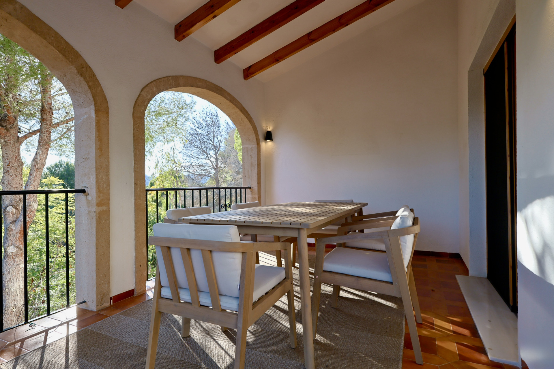 Terrasse couverte avec arches en pierre naturelle, poutres en bois apparentes et coin repas extérieur offrant une vue sur la végétation.
