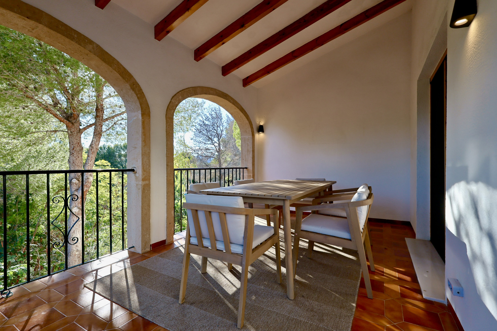 Terrasse couverte avec arches en pierre, poutres en bois apparentes et sol en terre cuite. Espace dînatoire extérieur offrant une vue sur la végétation environnante.