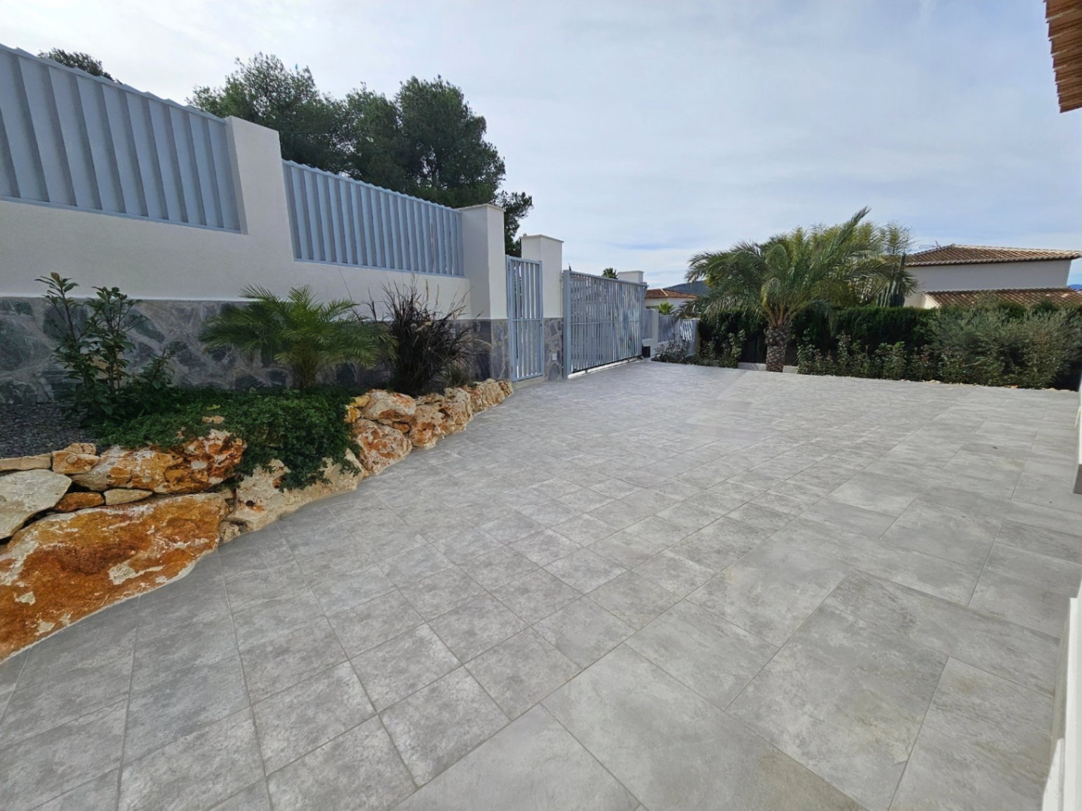 Allée pavée avec portail de sécurité gris et jardin de rocaille avec plantes méditerranéennes.