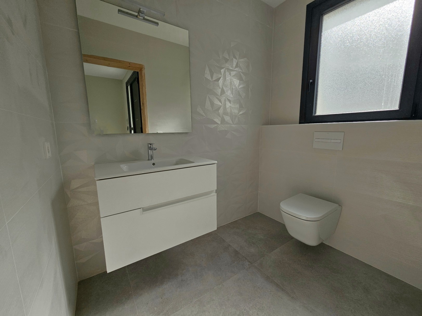 Détail d'une salle de bain moderne avec meuble-lavabo blanc suspendu, toilettes et carrelage géométrique.