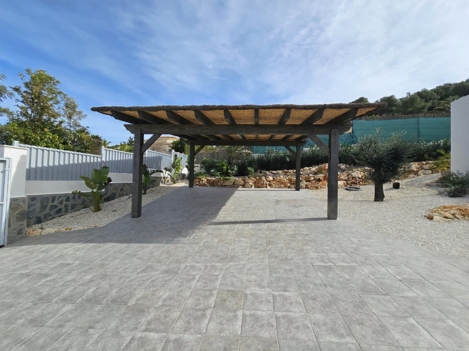 Pergola en bois avec toit de chaume sur sol carrelé gris dans la zone de stationnement.