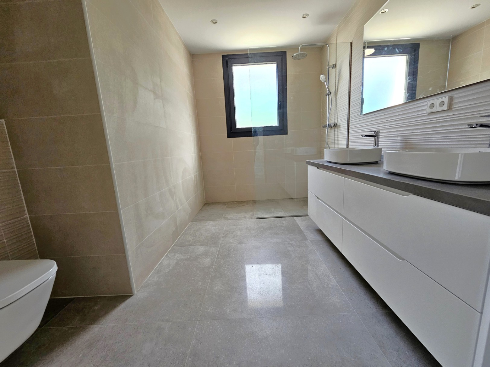 Salle de bain moderne avec carrelage crème, meuble-lavabo blanc à double vasque et douche à paroi de verre.