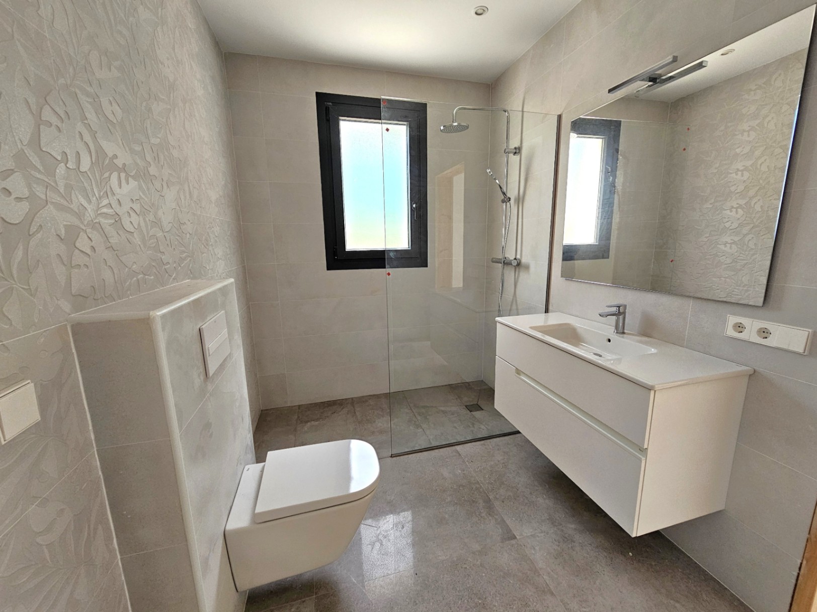 Salle de bain moderne avec douche à l'italienne, meuble-lavabo suspendu blanc et mur à motif floral.