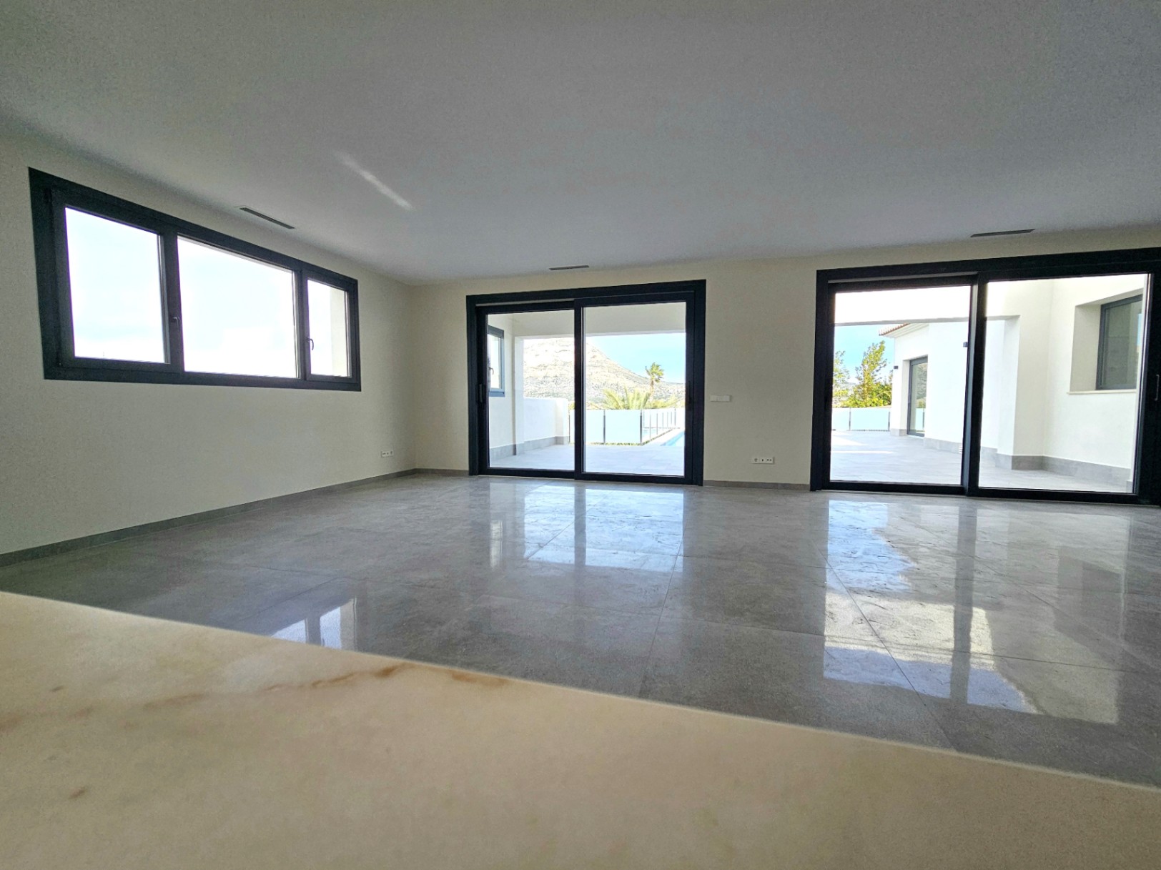 Salon spacieux avec carrelage en grès cérame et accès à la terrasse extérieure par de grandes portes coulissantes.