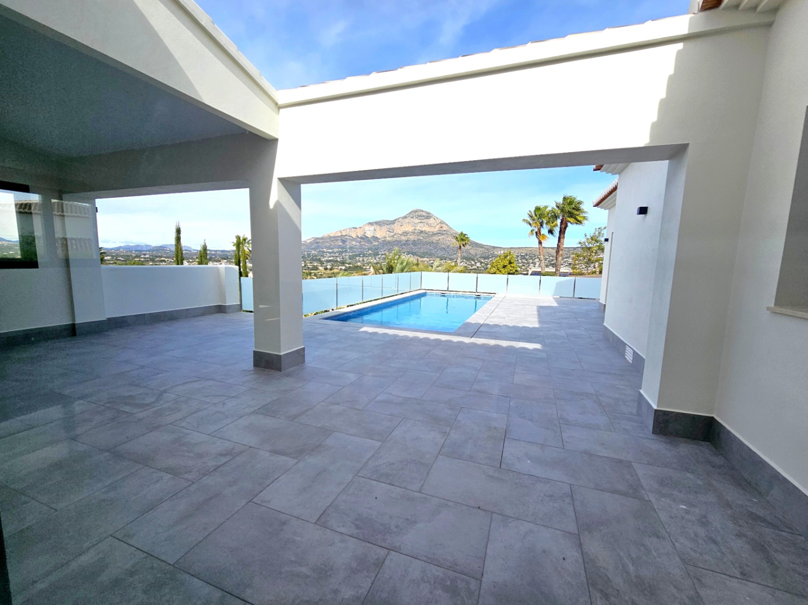 Terrasse couverte avec carrelage gris, vue sur la piscine et le Montgó.