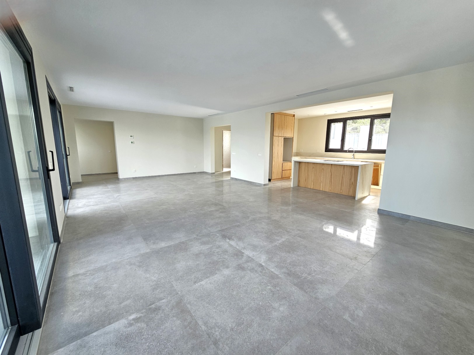 Vaste espace de vie avec carrelage en grès cérame et cuisine ouverte avec îlot central en bois clair.