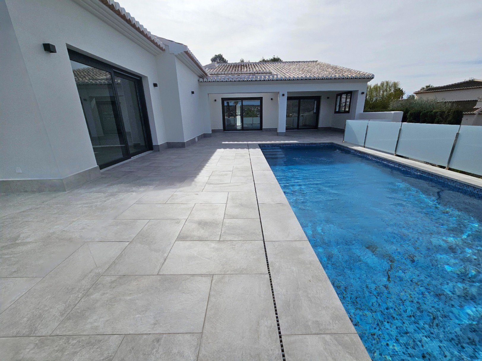 Vue de la terrasse pavée avec piscine et garde-corps en verre.