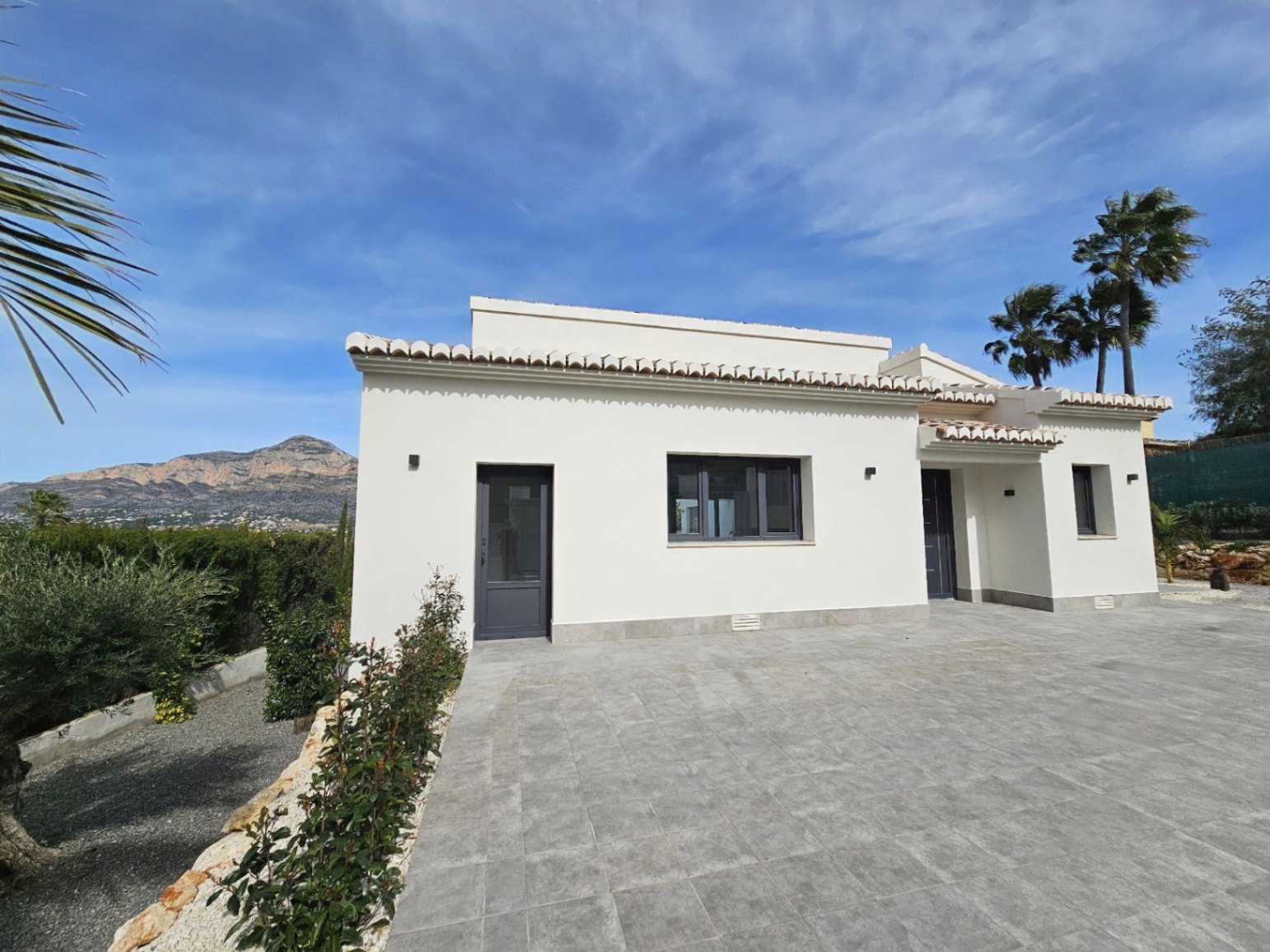 Vue extérieure de la villa avec façade blanche, tuiles et accès pavé gris.