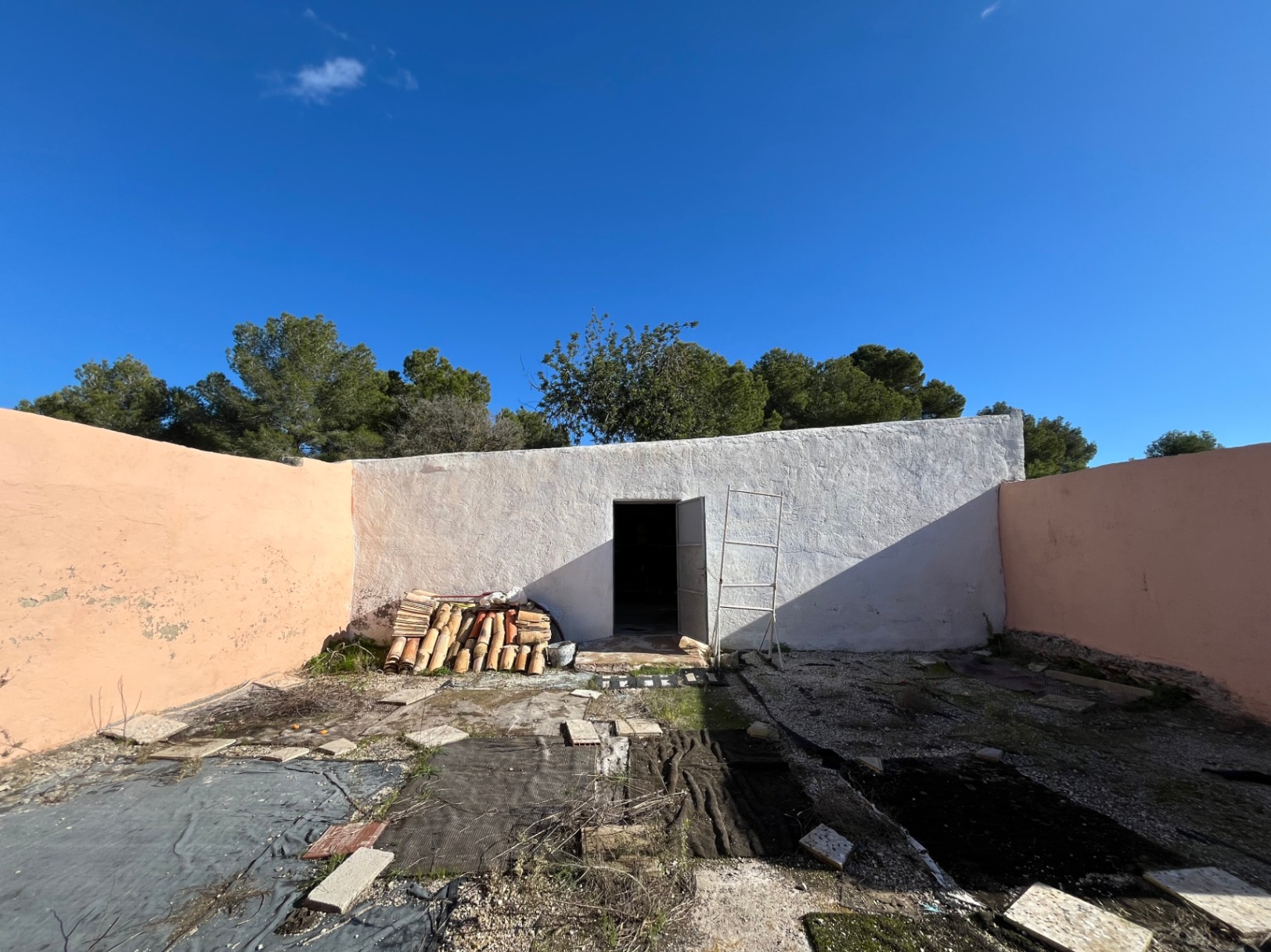 Cour intérieure fermée avec dépendance blanchie à la chaux, piles de tuiles romaines traditionnelles et murs d'enceinte de couleur ocre.