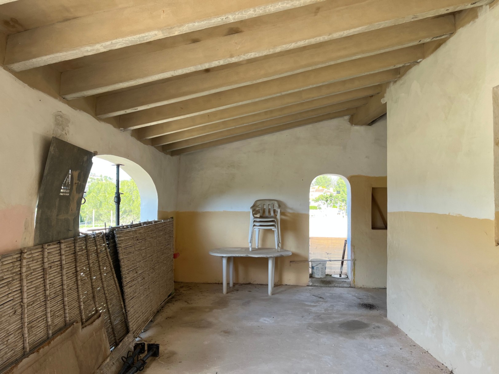Espace intérieur avec plafond incliné à poutres apparentes et ouvertures cintrées. Pièce dans son état d'origine, prête pour une rénovation complète.