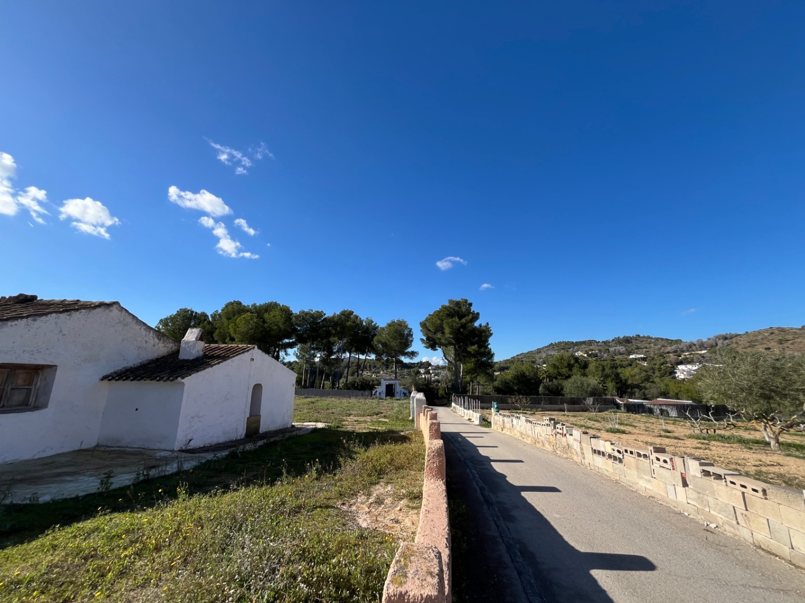Vue extérieure de la finca traditionnelle aux murs blancs et toit en tuiles, avec une allée pavée entourée de pins et d'un paysage méditerranéen.