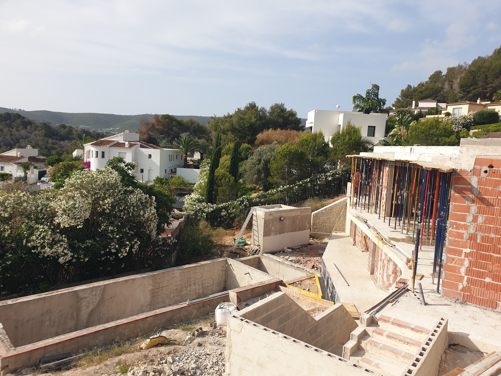 Chantier d'une villa présentant des fondations en béton, des murs en briques avec étais métalliques et l'excavation d'une piscine face à la vallée.