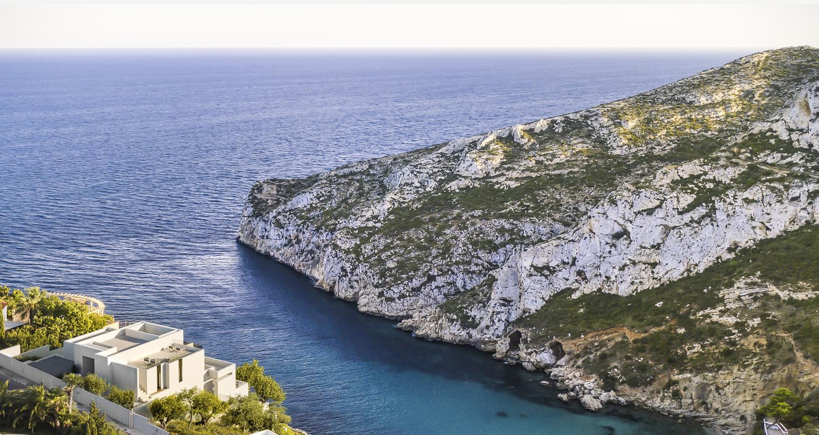 Villa moderne aux lignes cubiques située sur une falaise, offrant une vue imprenable sur une crique turquoise et des falaises calcaires à Jávea.
